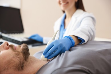 Photo of Sonographer conducting ultrasound examination of man's thyroid gland in clinic, closeup