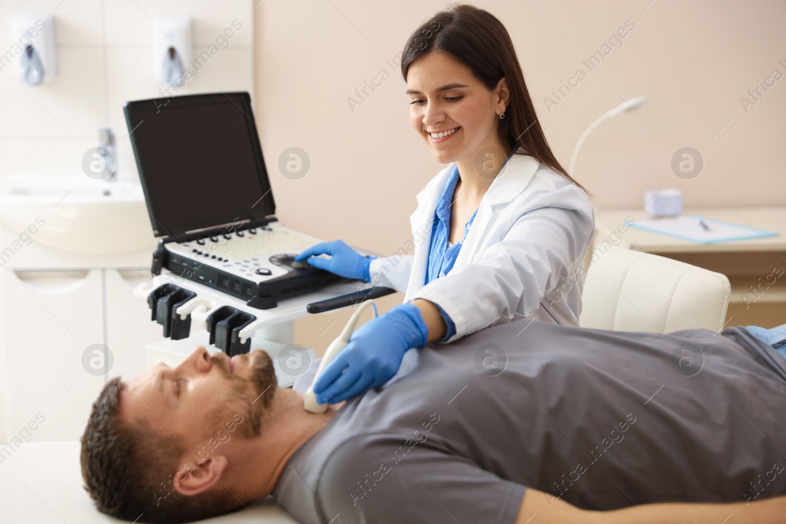 Photo of Sonographer conducting ultrasound examination of man's thyroid gland in clinic