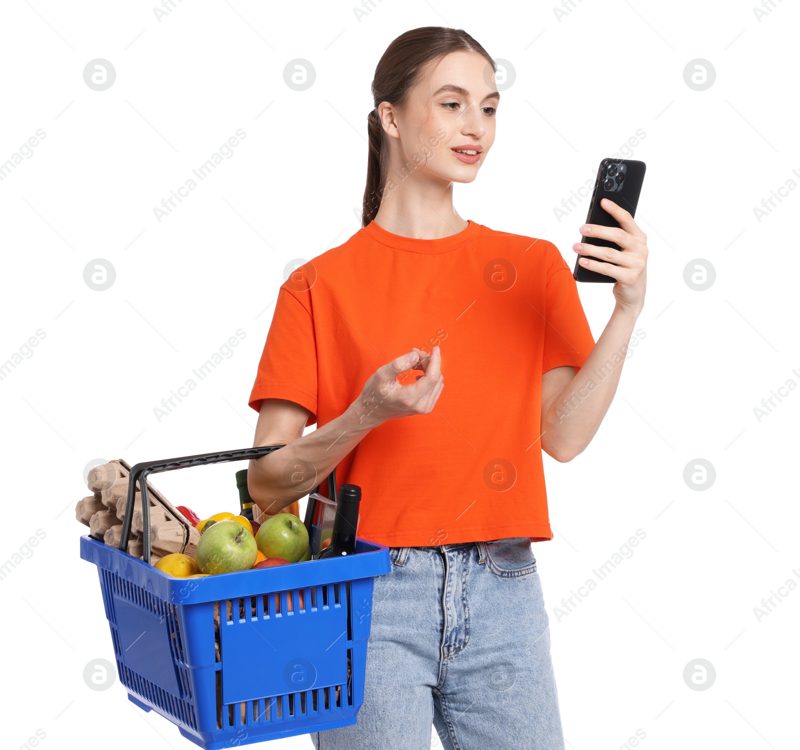 Woman with shopping basket full of products and smartphone on white background Photo of Woman with shopping basket full of products and smartphone on white background