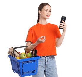 Photo of Woman with shopping basket full of products and smartphone on white background