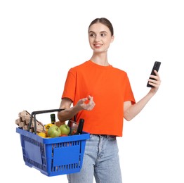 Photo of Woman with shopping basket full of products and smartphone on white background