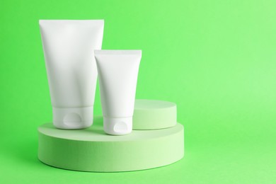 Photo of Stylish presentation of moisturizing body cream in tubes on light green background, closeup. Space for text