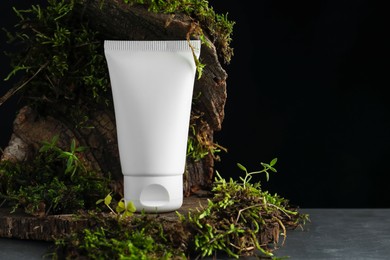 Photo of Tube of moisturizing body cream, tree bark and plants on grey table, closeup. Space for text