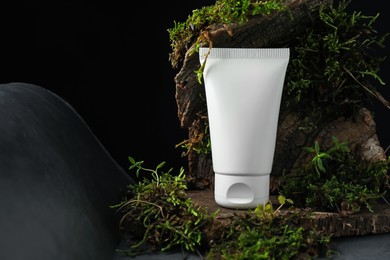 Photo of Tube of moisturizing body cream, tree bark and plants on grey table, closeup. Space for text