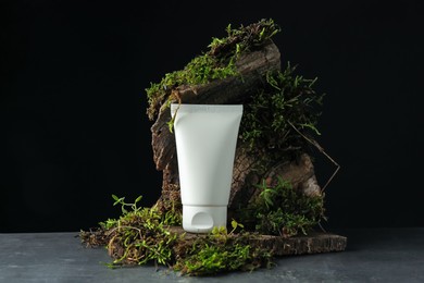 Photo of Tube of moisturizing body cream, tree bark and plants on grey table, closeup