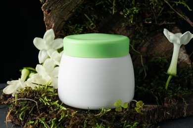 Photo of Jar of moisturizing body cream on tree bark with plants and flowers, closeup