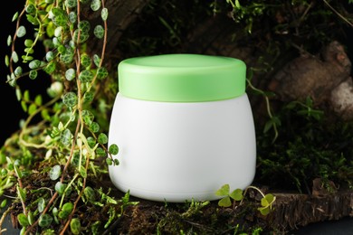 Photo of Jar of moisturizing body cream on tree bark with plants, closeup