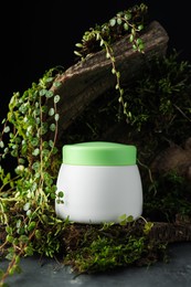 Photo of Jar of moisturizing body cream, tree bark and plants on grey table, closeup