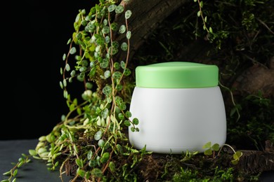 Photo of Jar of moisturizing body cream, tree bark and plants on grey table, closeup. Space for text