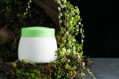 Photo of Jar of moisturizing body cream, tree bark and plants on grey table, closeup. Space for text