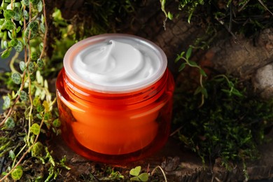 Photo of Jar of moisturizing body cream on tree bark with plants, closeup