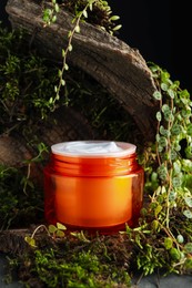 Photo of Jar of moisturizing body cream, tree bark and plants on grey table, closeup