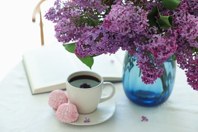 Photo of Bouquet of beautiful lilac flowers, coffee, dessert and book on white table indoors
