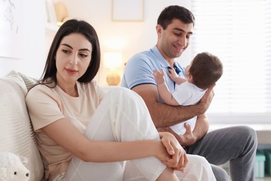 Photo of Woman suffering from postpartum depression and her husband with baby on sofa at home