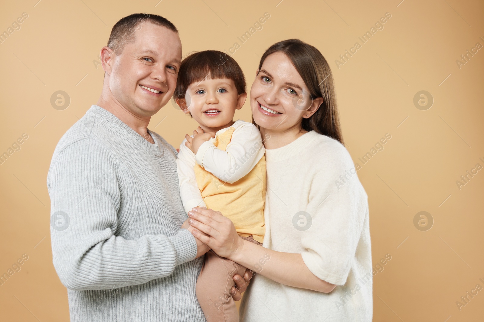 Happy parents and their baby boy on beige background. Lovely family Photo of Happy parents and their baby boy on beige background. Lovely family