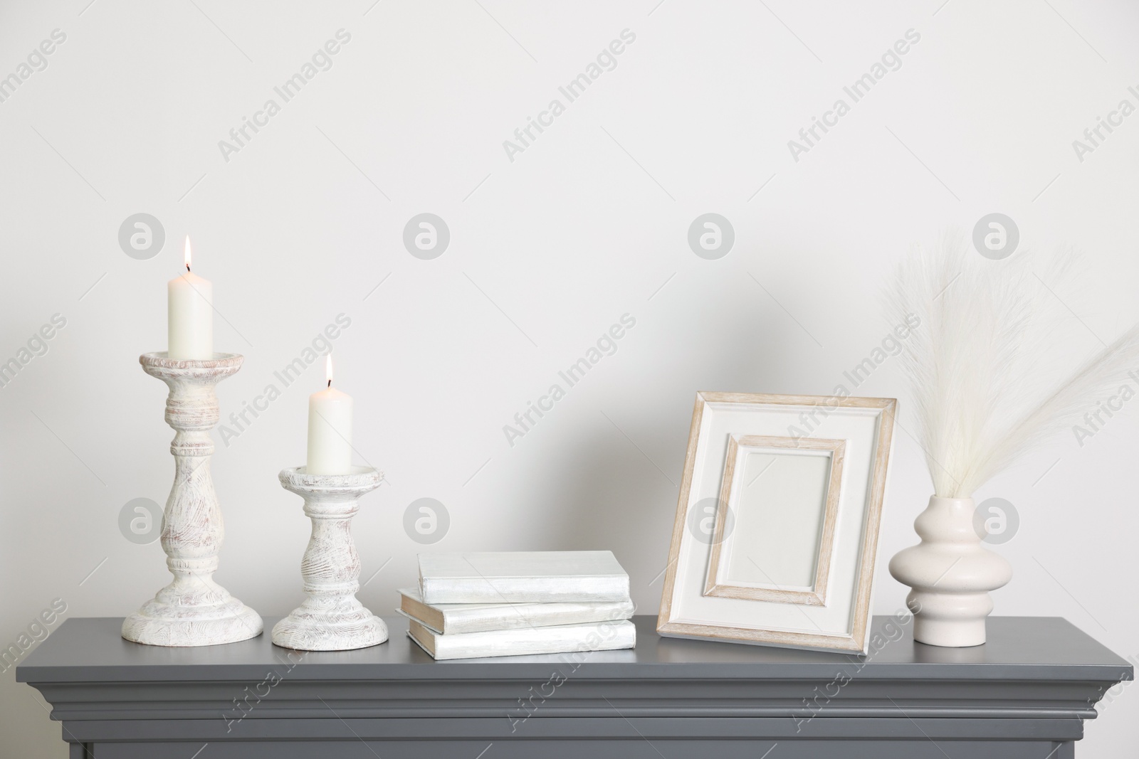 Stylish candlesticks with burning candles and other decor on fireplace near white wall indoors Photo of Stylish candlesticks with burning candles and other decor on fireplace near white wall indoors