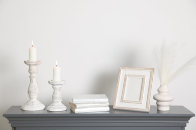 Photo of Stylish candlesticks with burning candles and other decor on fireplace near white wall indoors