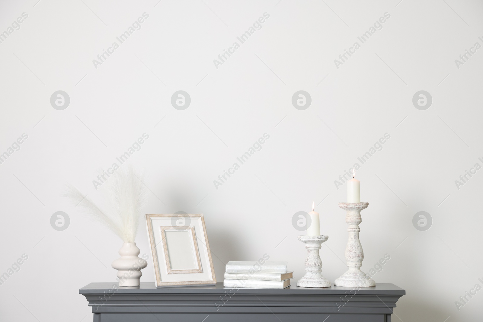 Stylish candlesticks with burning candles and other decor on fireplace near white wall indoors Photo of Stylish candlesticks with burning candles and other decor on fireplace near white wall indoors