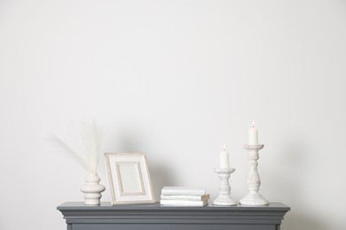 Photo of Stylish candlesticks with burning candles and other decor on fireplace near white wall indoors