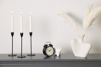 Photo of Stylish candlesticks with burning candles, other decor and alarm clock on fireplace near white wall indoors