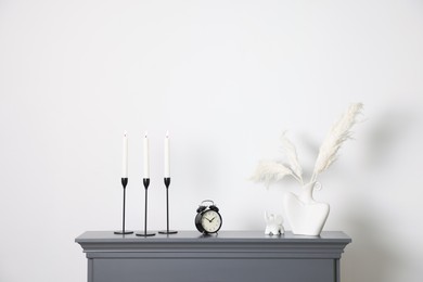 Photo of Stylish candlesticks with burning candles, other decor and alarm clock on fireplace near white wall indoors