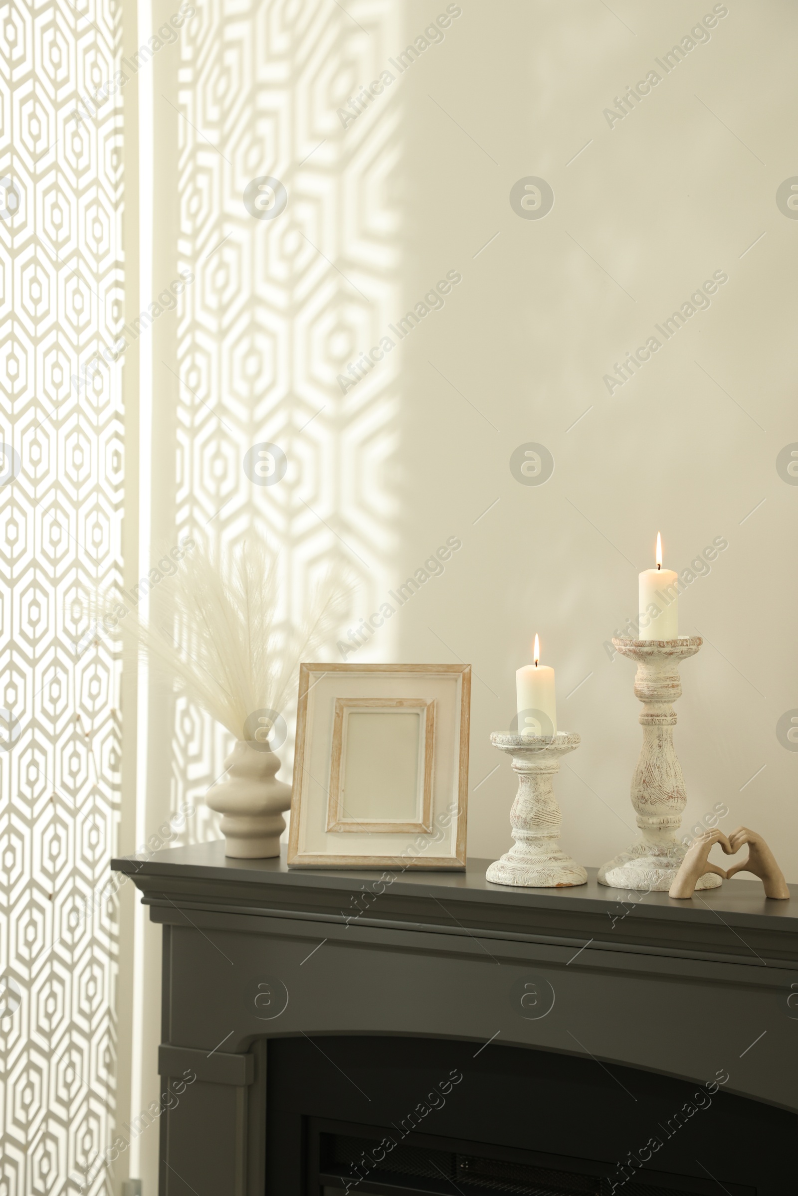 Stylish candlesticks with burning candles and other decor on fireplace near white wall indoors Photo of Stylish candlesticks with burning candles and other decor on fireplace near white wall indoors