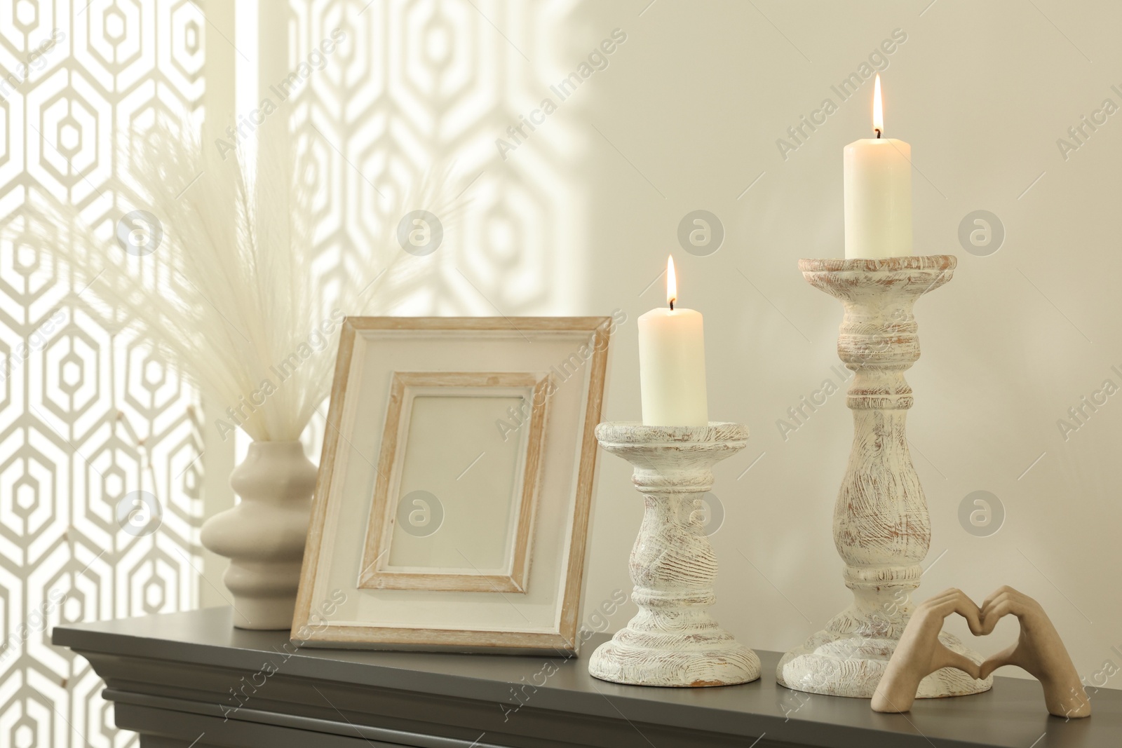 Stylish candlesticks with burning candles and other decor on fireplace near white wall indoors Photo of Stylish candlesticks with burning candles and other decor on fireplace near white wall indoors