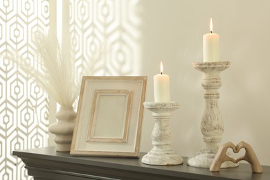 Photo of Stylish candlesticks with burning candles and other decor on fireplace near white wall indoors