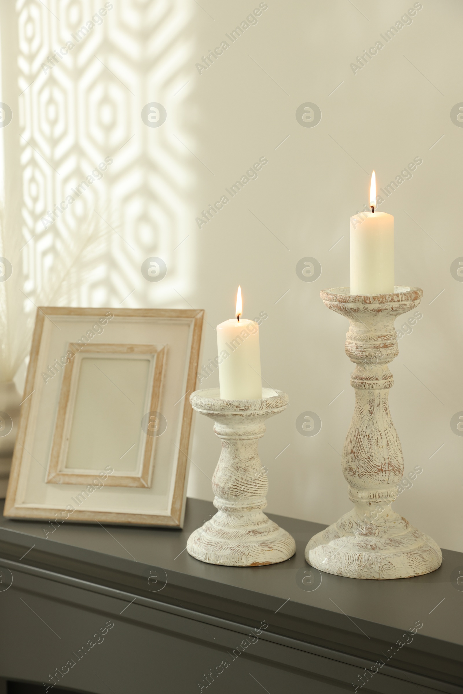 Photo of Stylish candlesticks with burning candles and other decor on fireplace near white wall indoors
