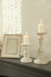 Photo of Stylish candlesticks with burning candles and other decor on fireplace near white wall indoors