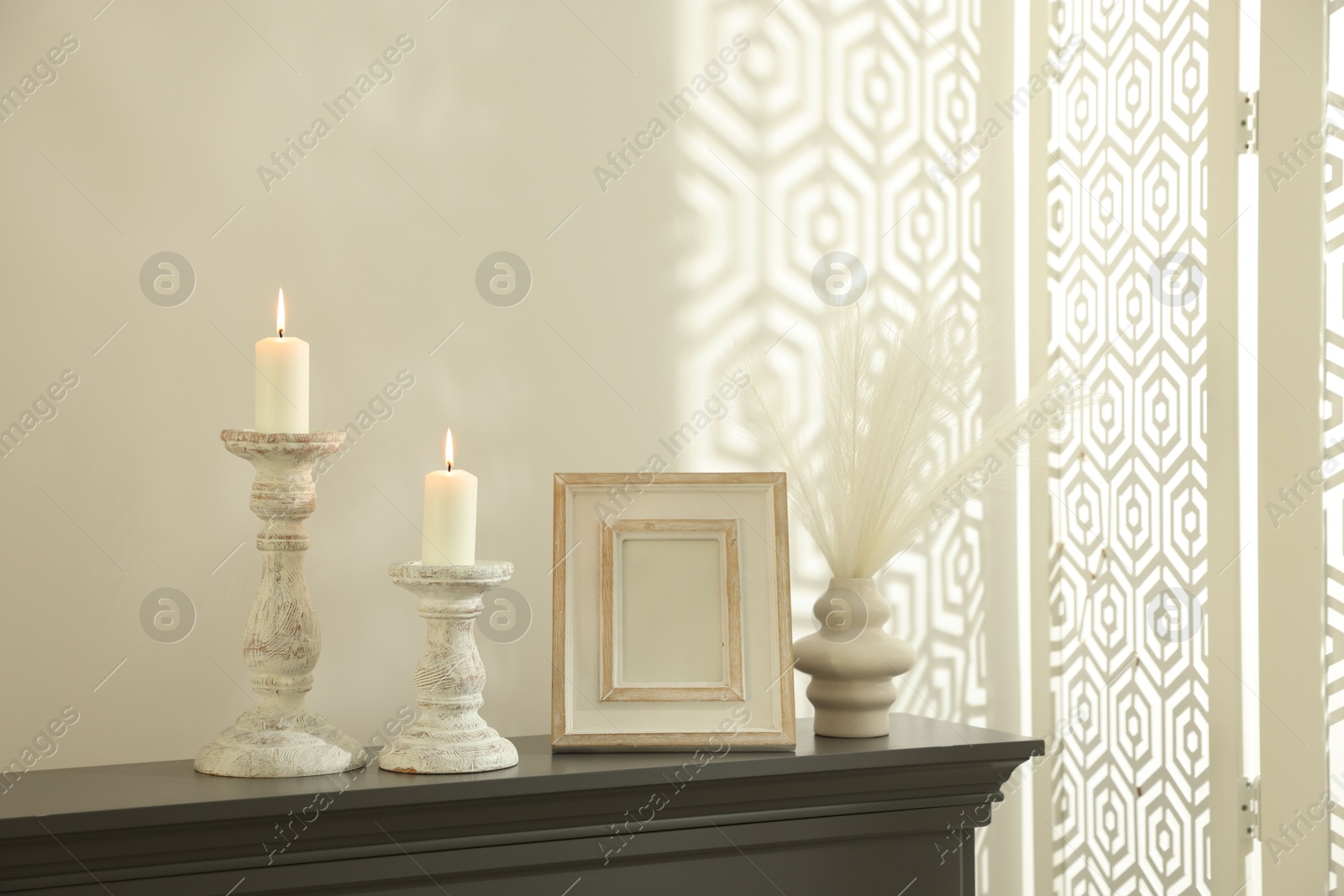 Stylish candlesticks with burning candles and other decor on fireplace near white wall indoors Photo of Stylish candlesticks with burning candles and other decor on fireplace near white wall indoors
