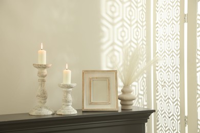 Photo of Stylish candlesticks with burning candles and other decor on fireplace near white wall indoors