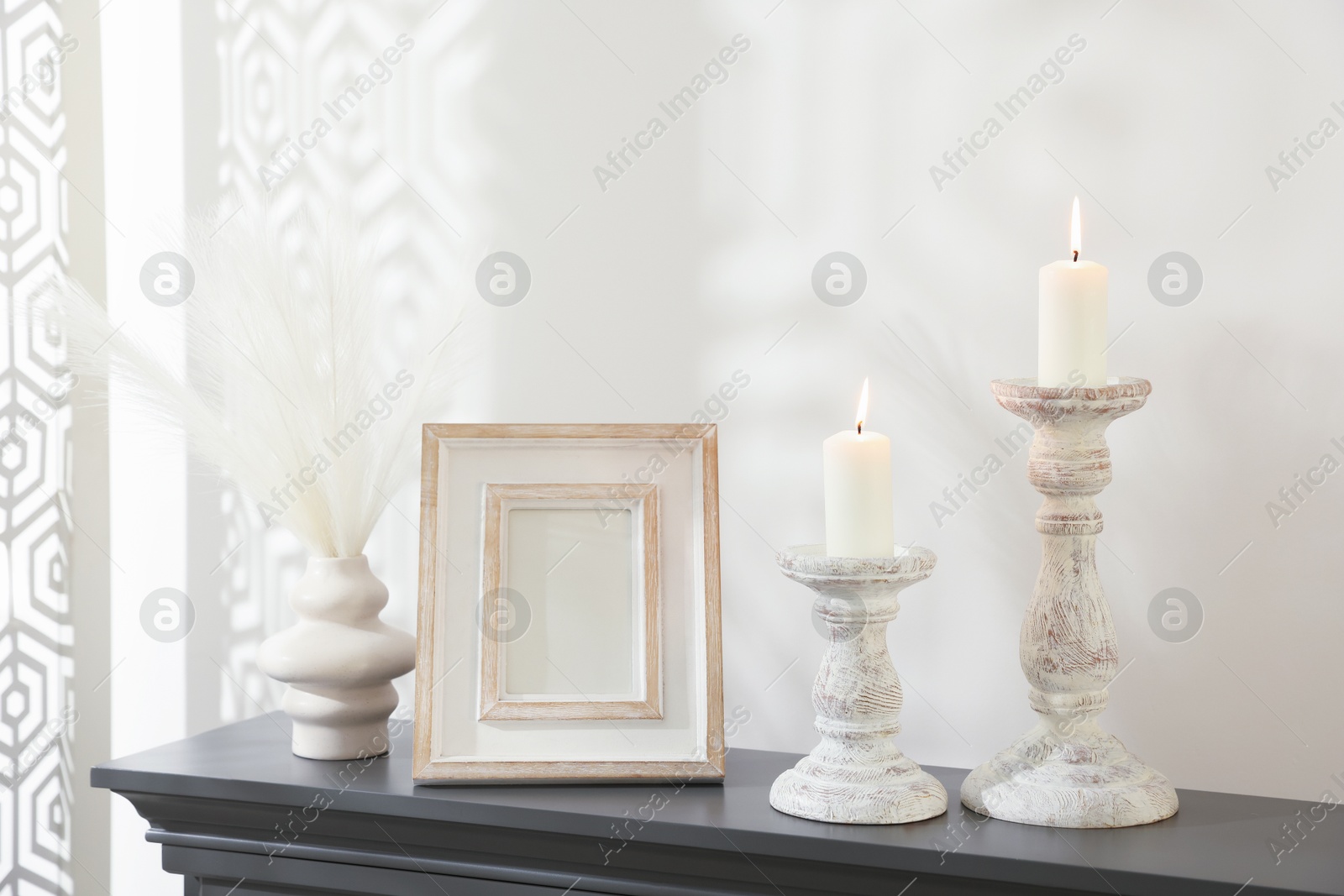 Stylish candlesticks with burning candles and other decor on fireplace near white wall indoors Photo of Stylish candlesticks with burning candles and other decor on fireplace near white wall indoors
