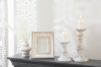 Photo of Stylish candlesticks with burning candles and other decor on fireplace near white wall indoors