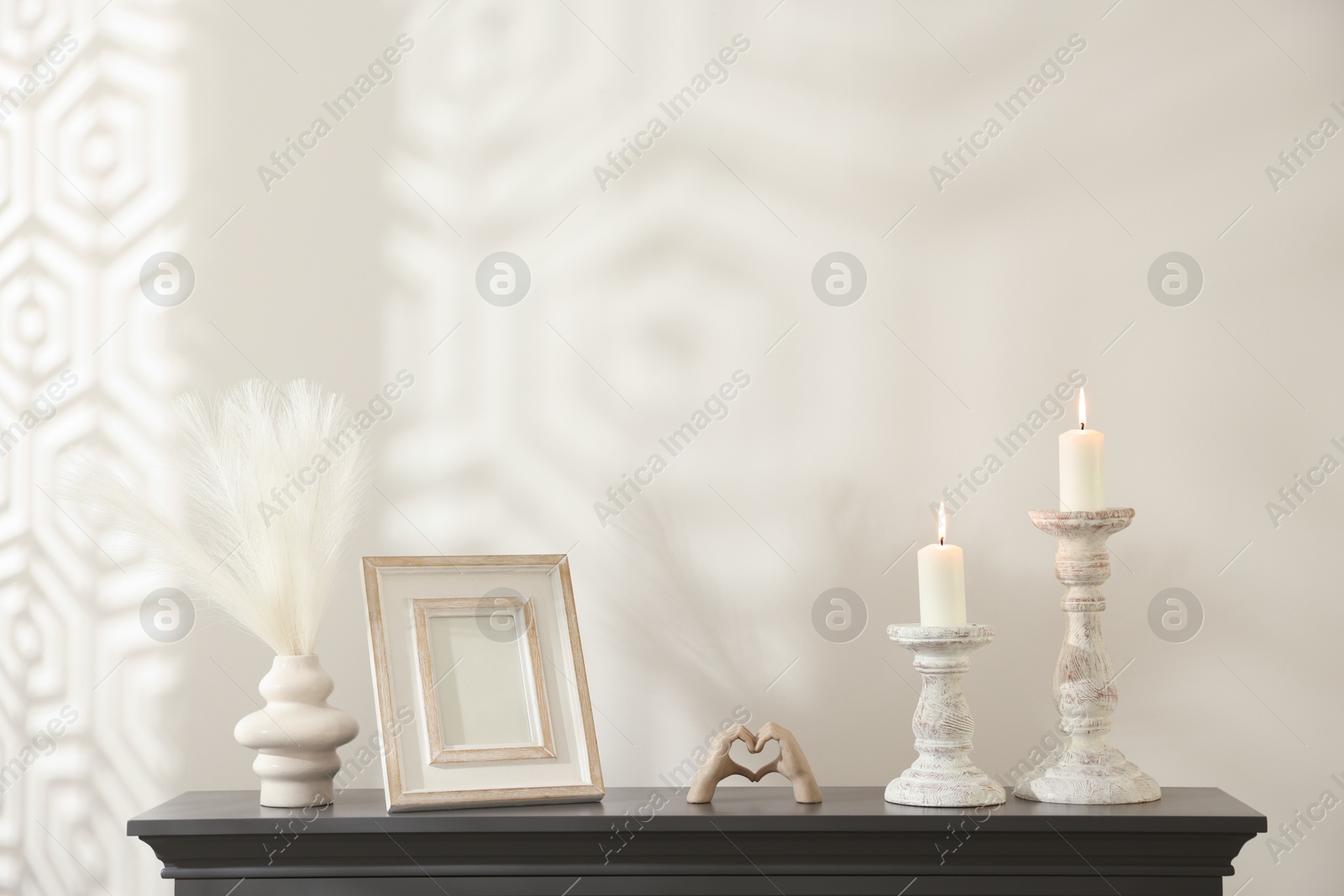 Stylish candlesticks with burning candles and other decor on fireplace near white wall indoors Photo of Stylish candlesticks with burning candles and other decor on fireplace near white wall indoors