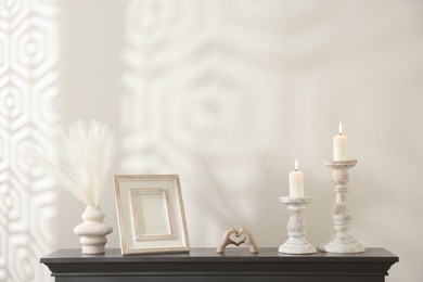 Photo of Stylish candlesticks with burning candles and other decor on fireplace near white wall indoors