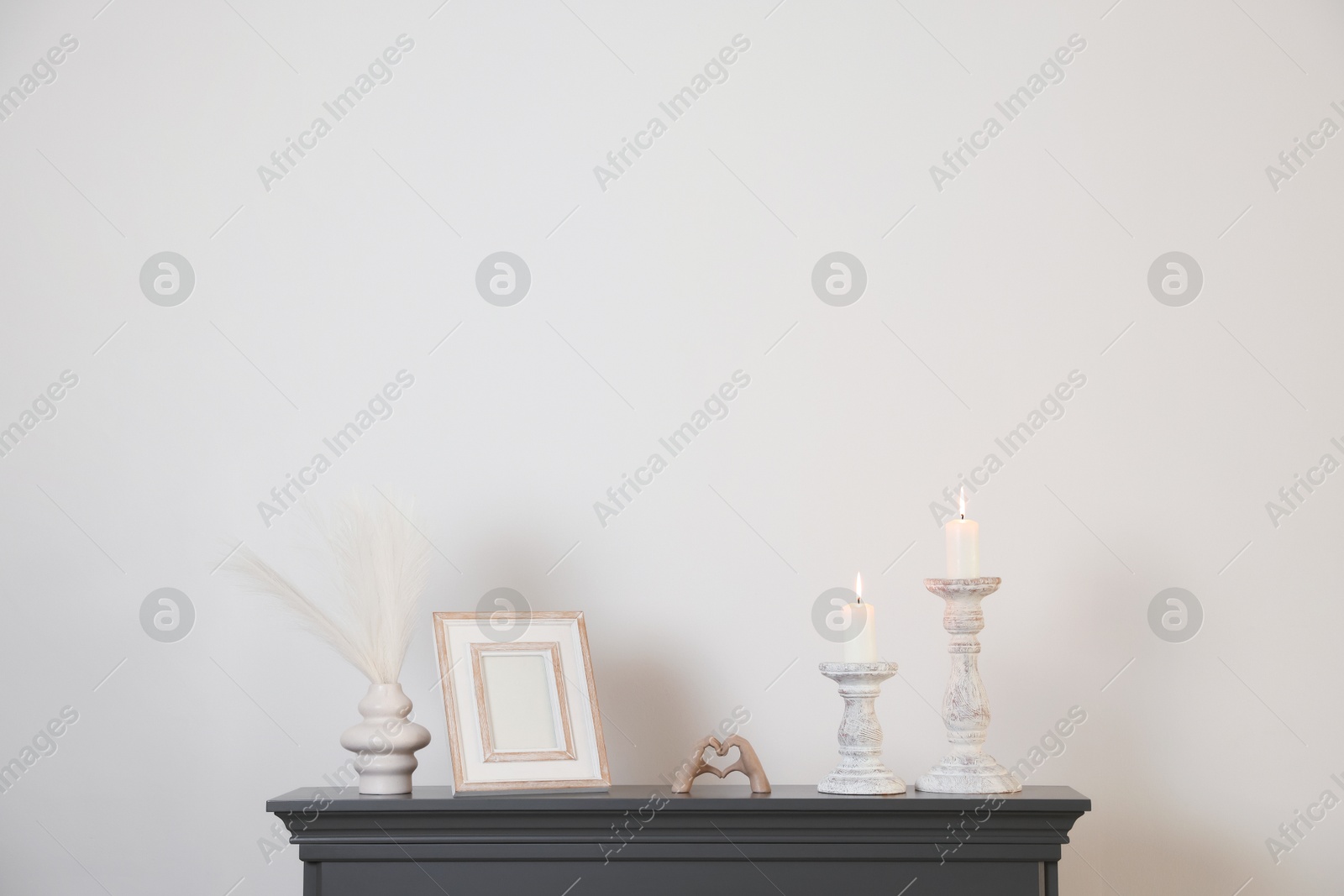 Stylish candlesticks with burning candles and other decor on fireplace near white wall indoors Photo of Stylish candlesticks with burning candles and other decor on fireplace near white wall indoors