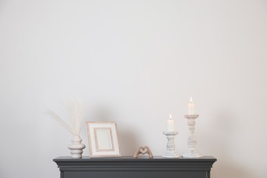 Photo of Stylish candlesticks with burning candles and other decor on fireplace near white wall indoors