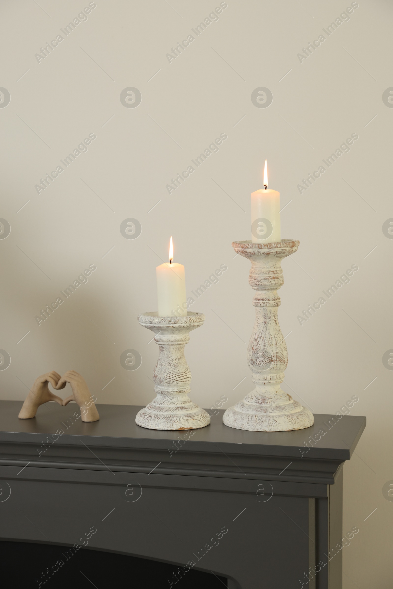 Stylish candlesticks with burning candles and other decor on fireplace near white wall indoors Photo of Stylish candlesticks with burning candles and other decor on fireplace near white wall indoors