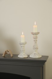 Photo of Stylish candlesticks with burning candles and other decor on fireplace near white wall indoors