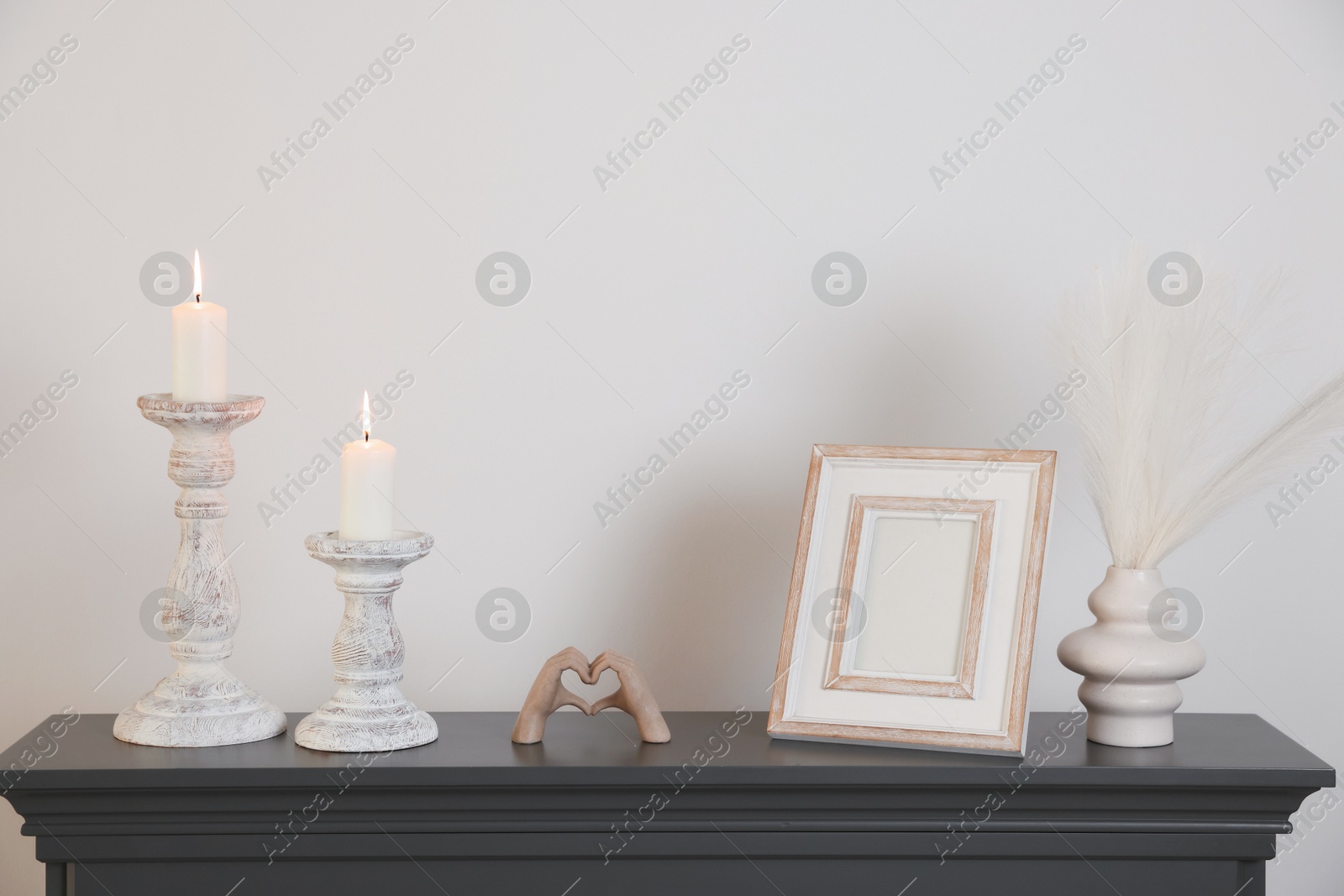 Stylish candlesticks with burning candles and other decor on fireplace near white wall indoors Photo of Stylish candlesticks with burning candles and other decor on fireplace near white wall indoors