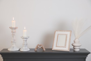 Photo of Stylish candlesticks with burning candles and other decor on fireplace near white wall indoors