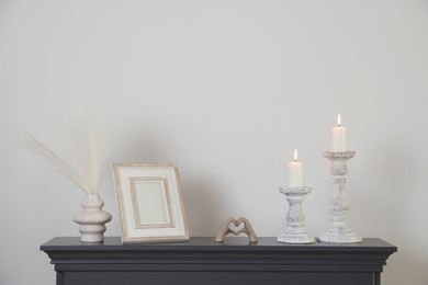 Photo of Stylish candlesticks with burning candles and other decor on fireplace near white wall indoors