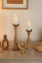 Photo of Stylish candlesticks with burning candles and other decor on cabinet near beige wall indoors