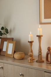 Photo of Stylish candlesticks with burning candles and other decor on cabinet near beige wall indoors