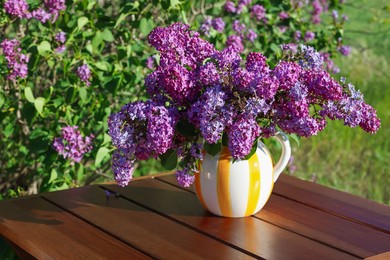 Photo of Beautiful lilac flowers in vase on wooden table in garden