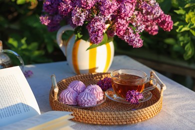 Photo of Beautiful lilac flowers, tea, zephyrs and book on table in garden