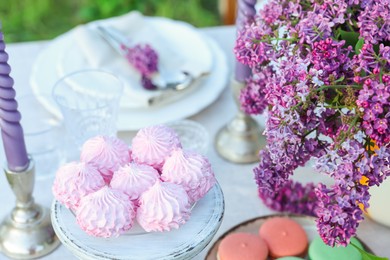 Photo of Beautiful lilac flowers, sweets, plates, cutlery and candles on table in garden, closeup