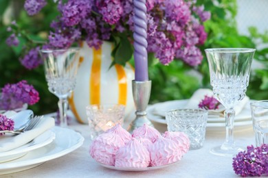 Photo of Beautiful lilac flowers, zephyrs, plates, cutlery, glasses and candles on table in garden, closeup