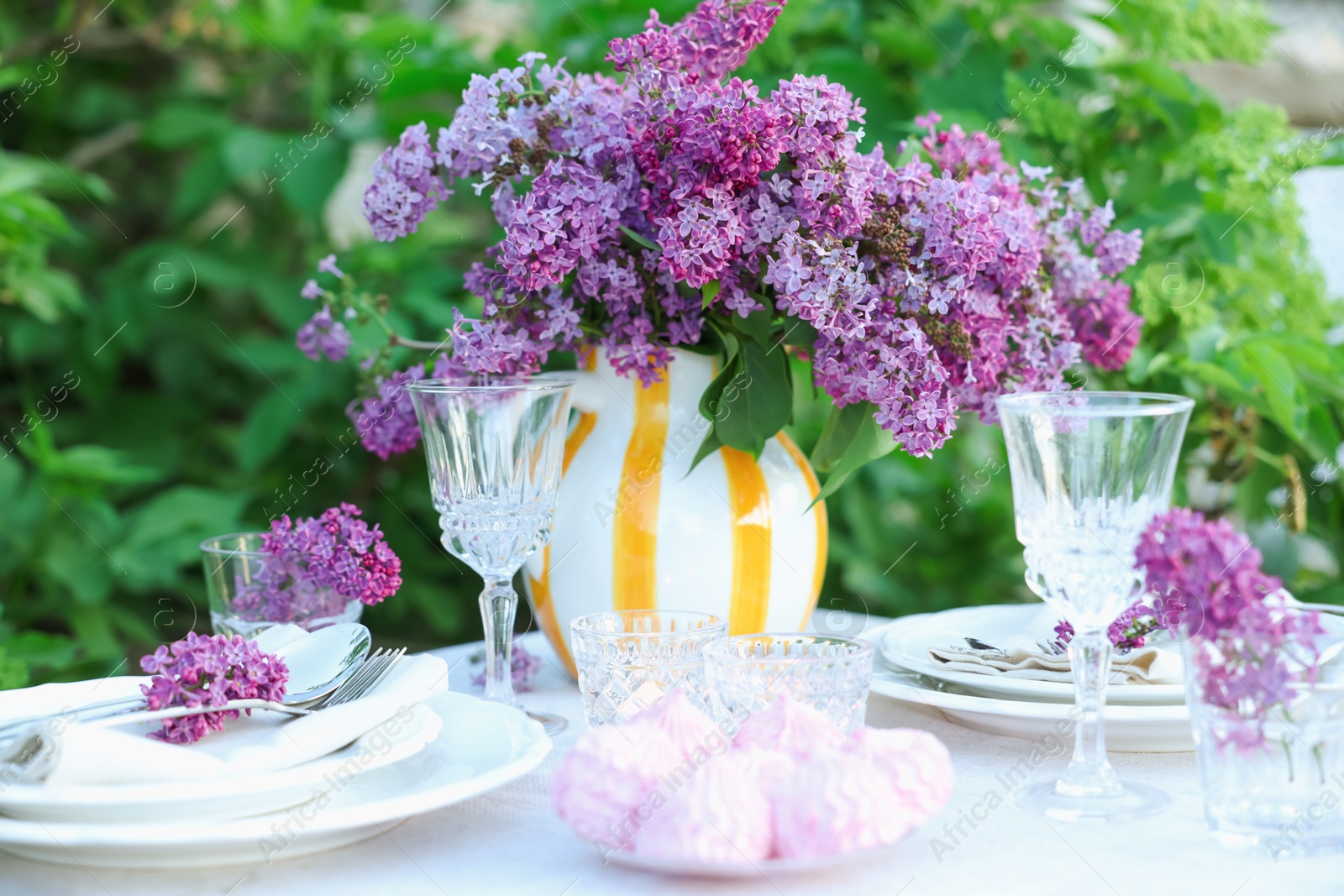 Beautiful lilac flowers, zephyrs, plates, cutlery and glasses on table in garden, closeup Photo of Beautiful lilac flowers, zephyrs, plates, cutlery and glasses on table in garden, closeup